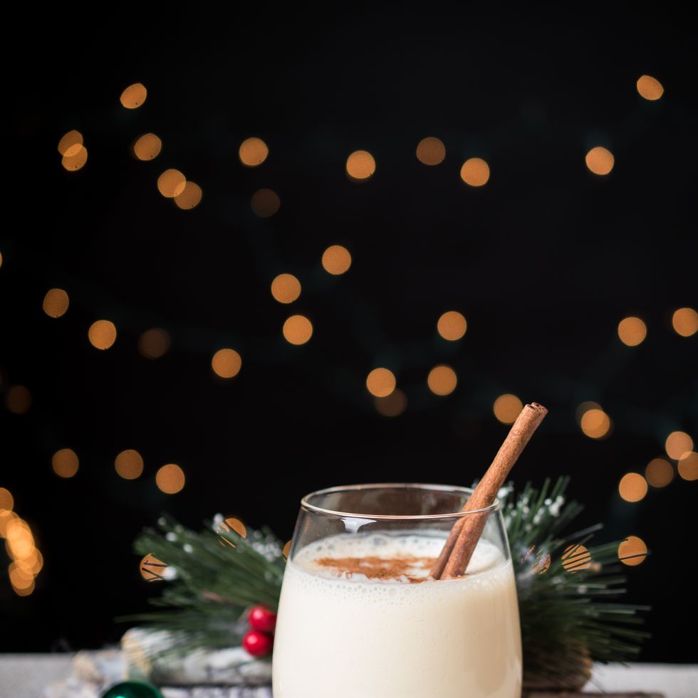 close up of eggnog in glass on a gray wooden table with christmas ornaments