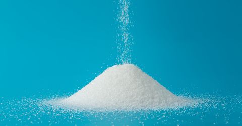 Close-Up Of Falling Sugar On Heap Against Blue Background