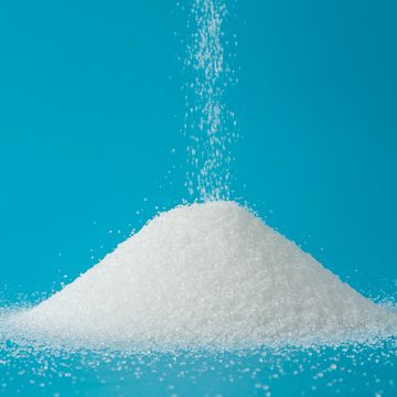 Close-Up Of Falling Sugar On Heap Against Blue Background