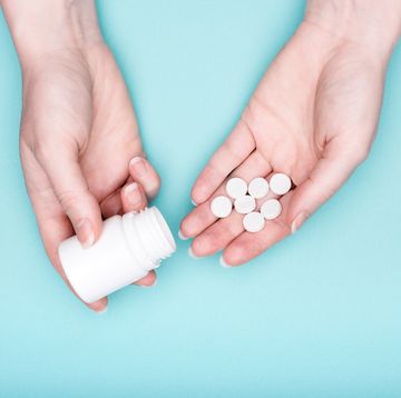 close up of female hands holding medication bottle and white pills over pastel blue background