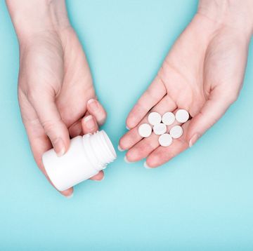 close up of female hands holding medication bottle and white pills over pastel blue background