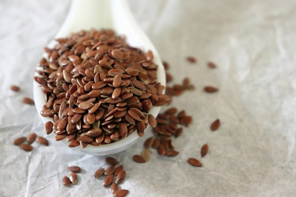 close up of flax seeds in a ceramic spoon on white background