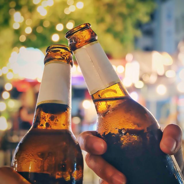 Close-Up Of Friends Toasting Beer Bottles At Night