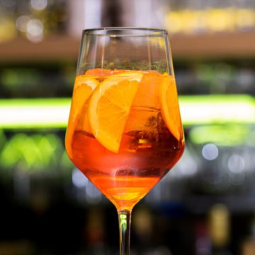 close up of glass with spritz orange color cocktail, ice cubes and slices of citrus fruit