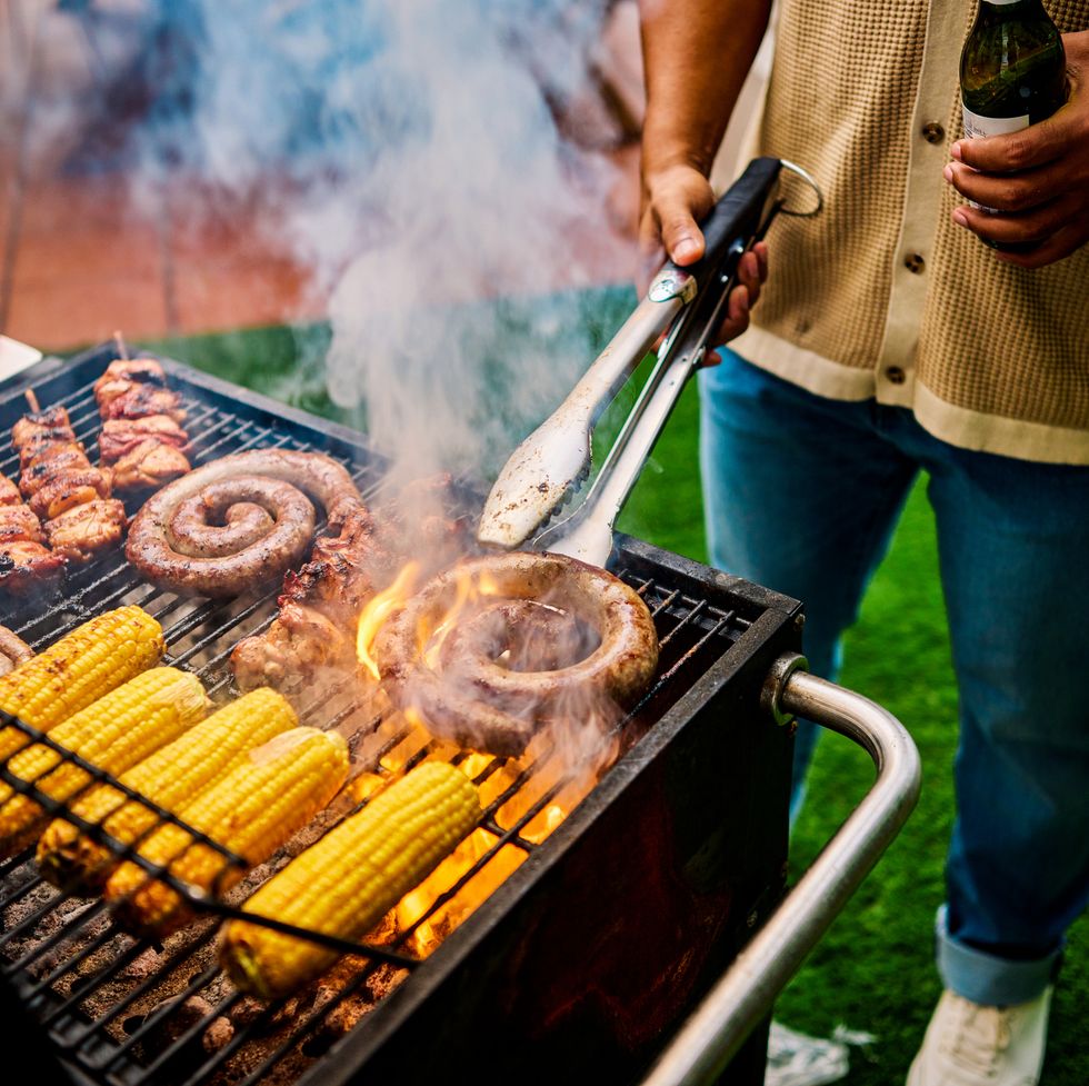 close up of grilling sausages and corn on an outdoor barbecue. social gathering with food. summer cooking and celebration concept.
