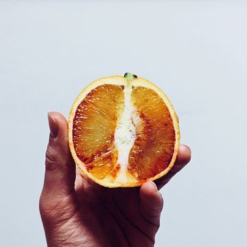 Close-Up Of Hand Holding Blood Orange Slice Against White Background