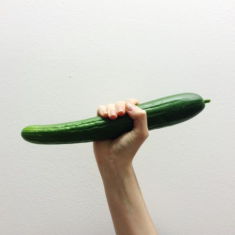 close up of hand holding cucumber over white background