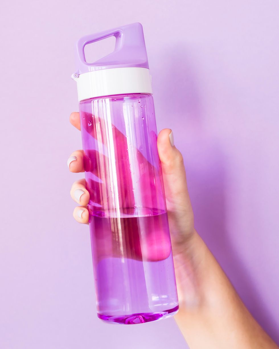 Close-Up Of Hand Holding Water Bottle Against Colored Background