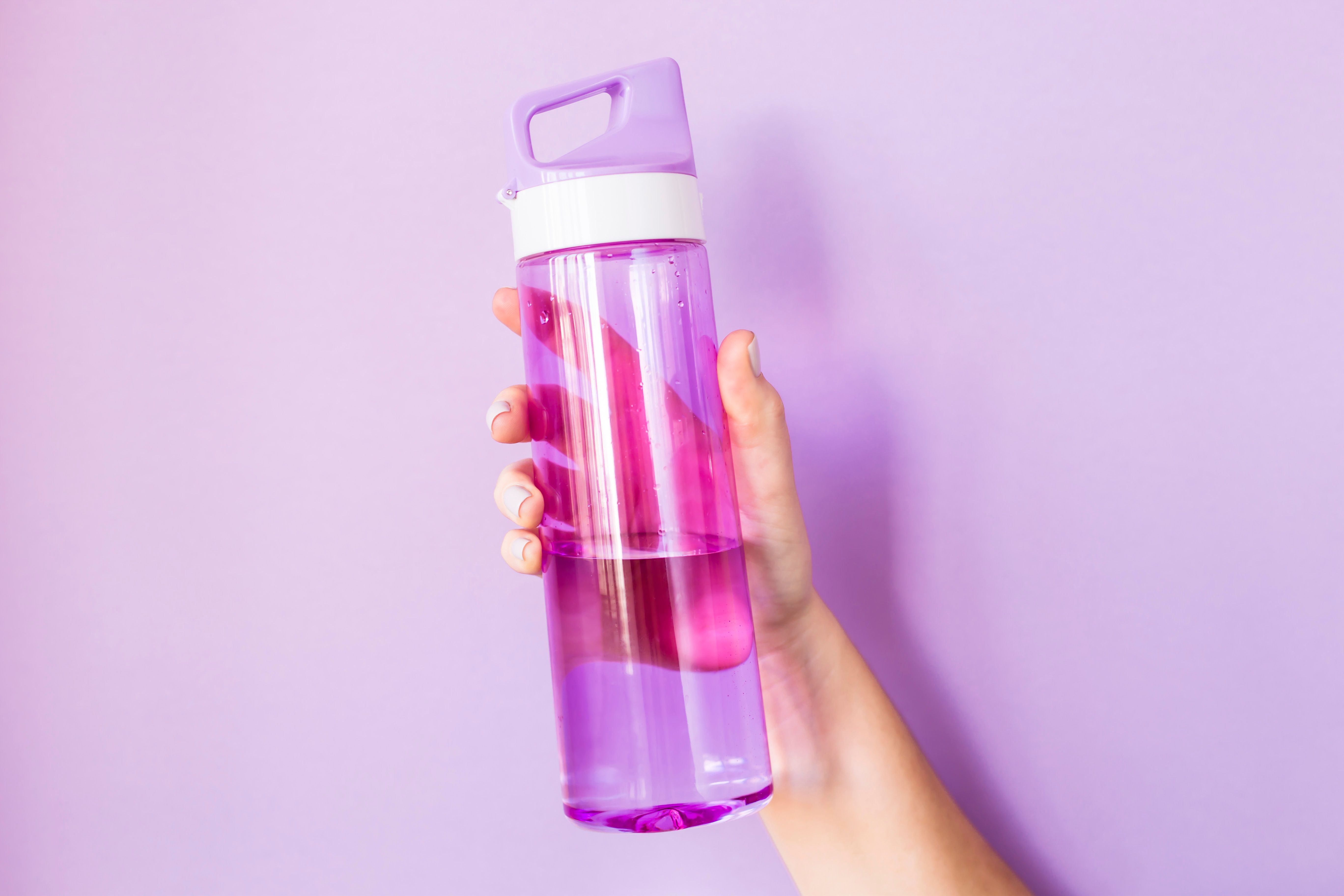 Close-Up Of Hand Holding Water Bottle Against Colored Background