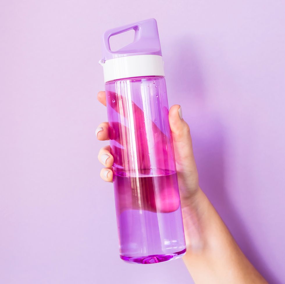 Close-Up Of Hand Holding Water Bottle Against Colored Background