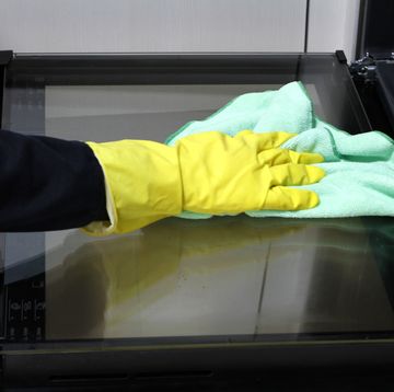 close up of hand with rubber glove cleaning oven with rag