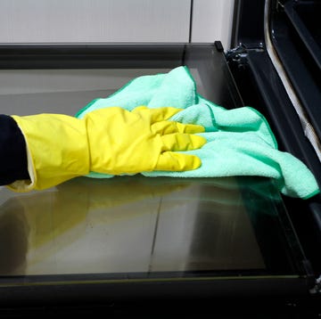 close up of hand with rubber glove cleaning oven with rag