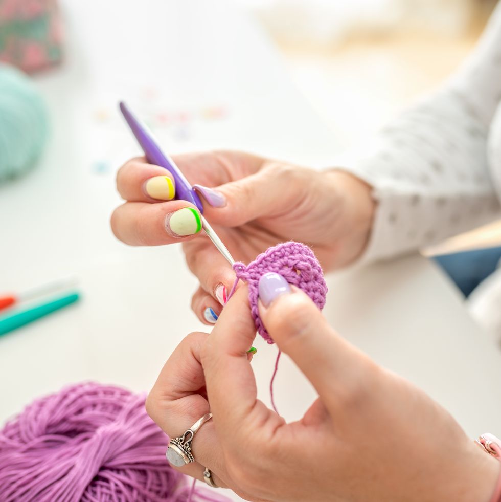 close up of hands crocheting with purple yarn in a creative workspace