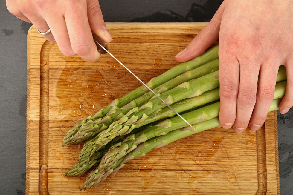Close-Up Of Hands Cutting Asparagus On Board