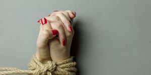 close up of hands tied with rope on gray background