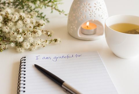 close up of handwritten gratitude text with notebook, pen, cup of tea, flowers and oil burner l