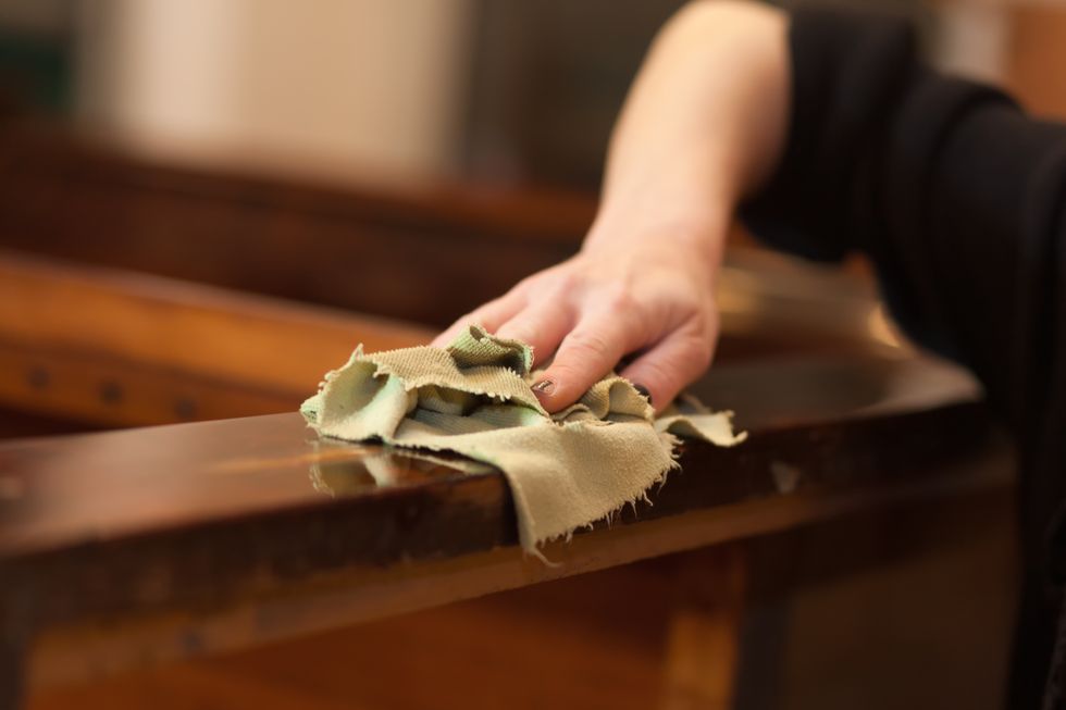 human hand wiping down a wooden surface with a rag and liquid sandpaper