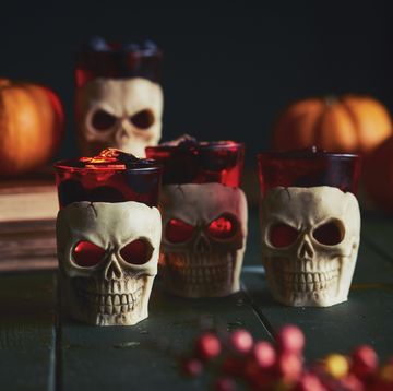 close up of human skull candles and orange pumpkins on a table