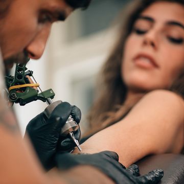 Close-Up Of Mam Making Tattoo On Woman Hand