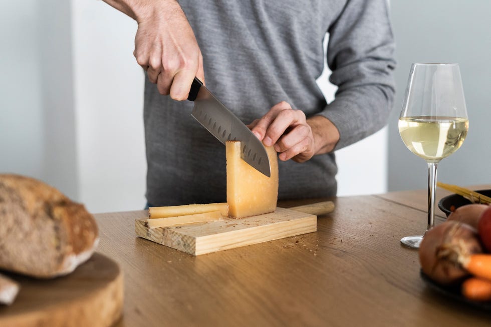 close up of man cutting cheese on kitchen counter