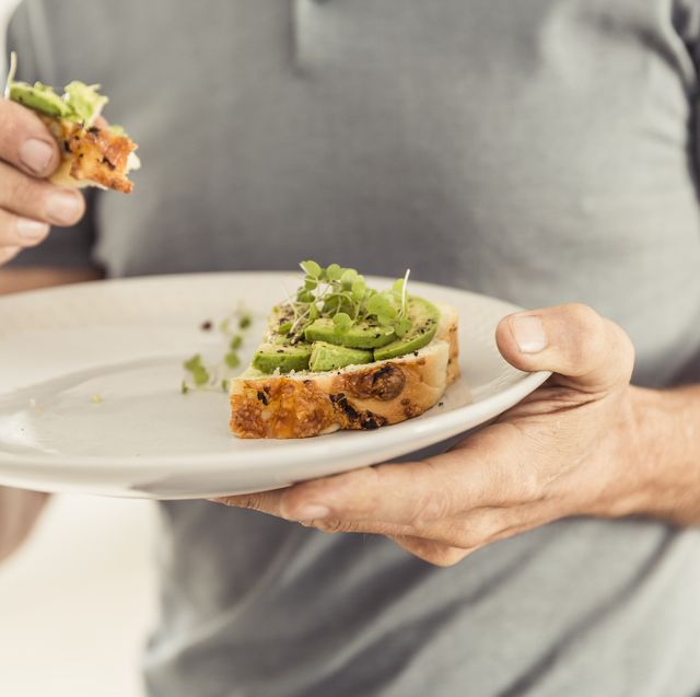 close up of man holding a plate with a healthy avocado bread