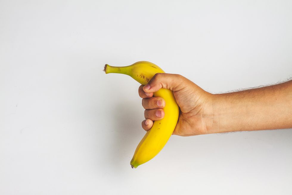 Close-Up Of Man Holding Banana Against White Background