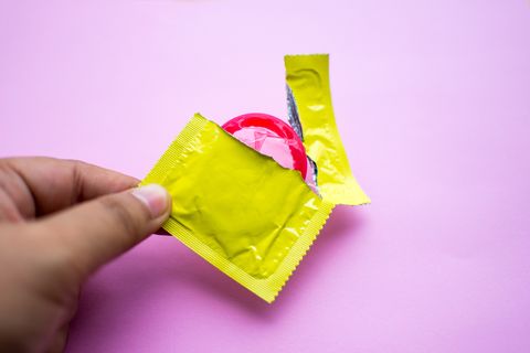 close up of man holding condom over pink background