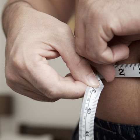 close up of man measuring waist with tape measure
