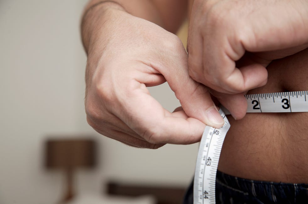 close up of man measuring waist with tape measure