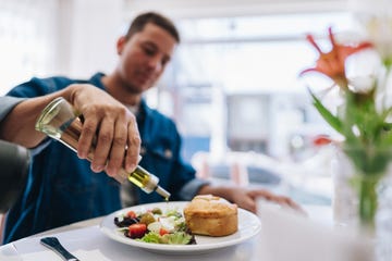 close up of man pouring olive oil on salad at restaurant