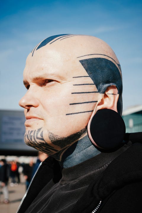 close up of man with tattoos and ear plug against sky