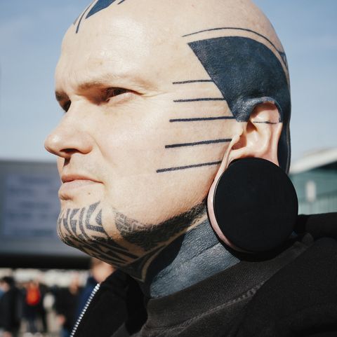 close up of man with tattoos and ear plug against sky