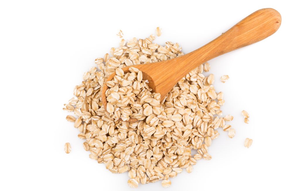 close up of oatmeal flakes in wooden spoon on white background