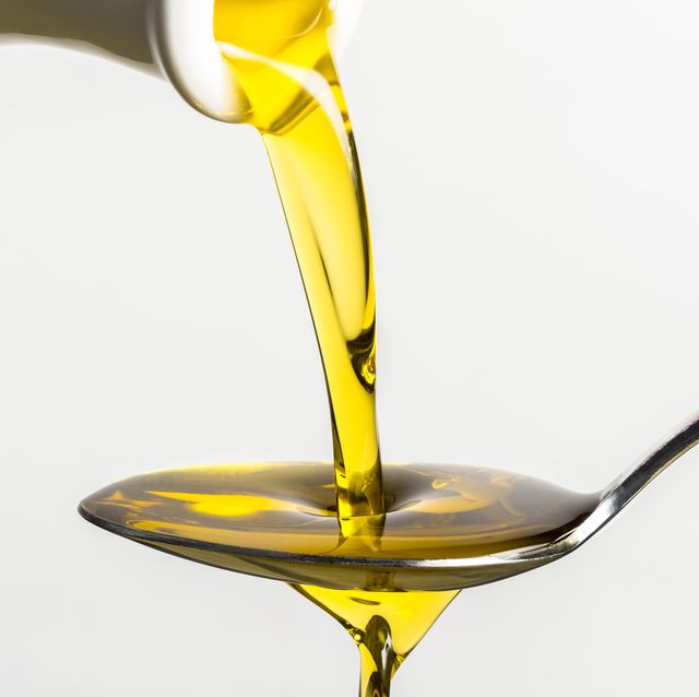 close up of olive oil pouring on spoon from container against white background