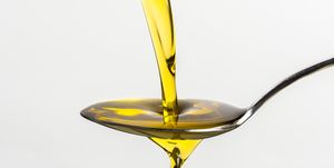 close up of olive oil pouring on spoon from container against white background
