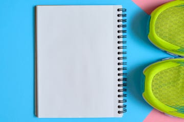 Close up of pair of sport shoes and blank empty notebook on pink and blue pastel background, copy space. Top view, flat lay. Sport, fitness concept, healthy lifestyle