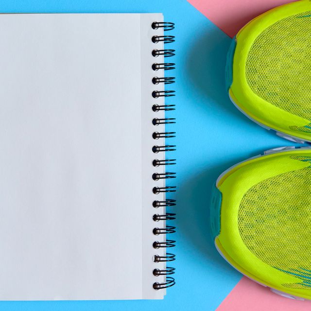 Close up of pair of sport shoes and blank empty notebook on pink and blue pastel background, copy space. Top view, flat lay. Sport, fitness concept, healthy lifestyle