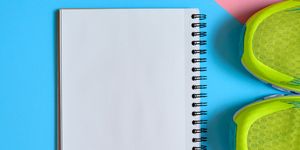 Close up of pair of sport shoes and blank empty notebook on pink and blue pastel background, copy space. Top view, flat lay. Sport, fitness concept, healthy lifestyle
