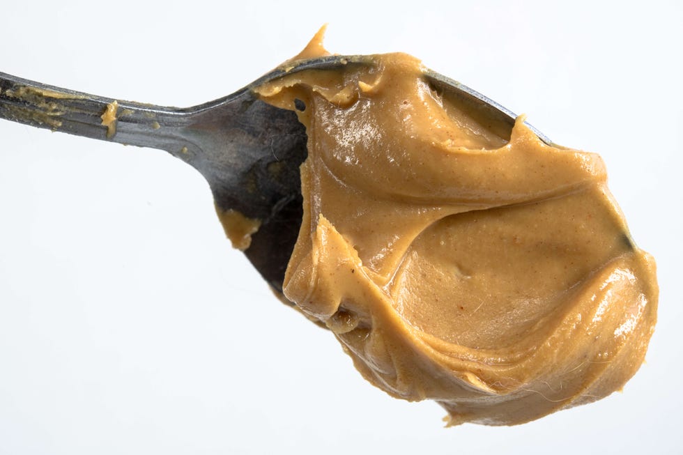 Close up of peanut butter in a spoon and over a white...