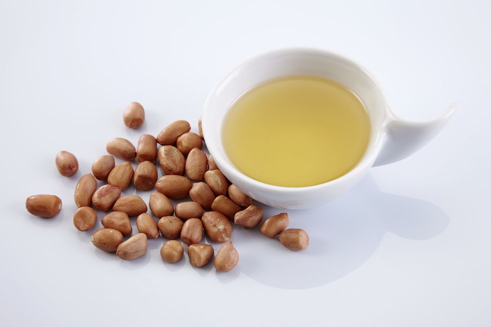 close up of peanuts and cooking oil over white background