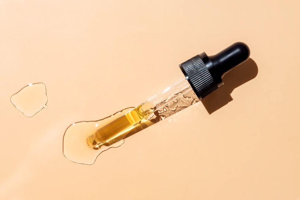 close up of pipette with pouring liquid serum and shadows on beige background trendy cosmetics shot with hard shadows
