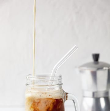 close up of 'proffee' protein and coffee in mason jar with reusable glass drinking straw on white background