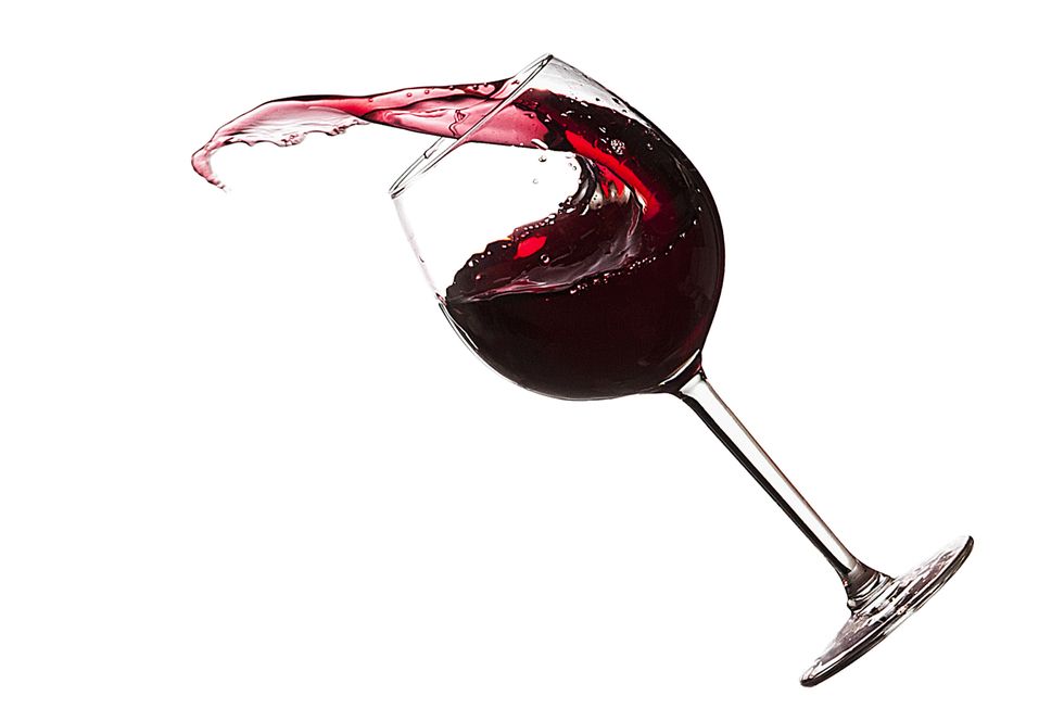 Close-Up Of Red Wine Spilling From Glass Over White Background