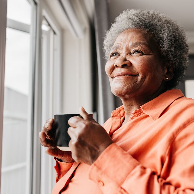 close up of senior woman holding mug, smiling beside window