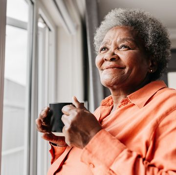 close up of senior woman holding mug, smiling beside window