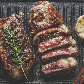 close up of sliced roasted medium rare barbecue steak with rosemary, roasted garlic and cutlery on rustic iron grill