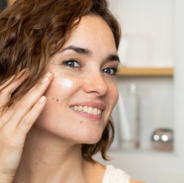 close up of smiling woman applying facial cream