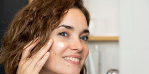 close up of smiling woman applying facial cream