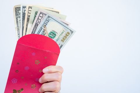 close up of someone holding a red envelope with american dollar banknotes inside in chinese culture, the color red is associated with energy, happiness and good luck