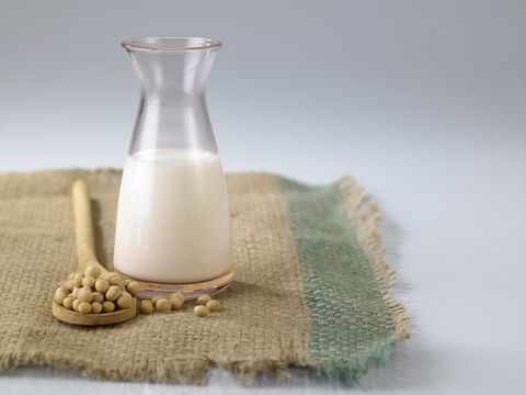 close up of soy milk with soybeans on burlap against white background